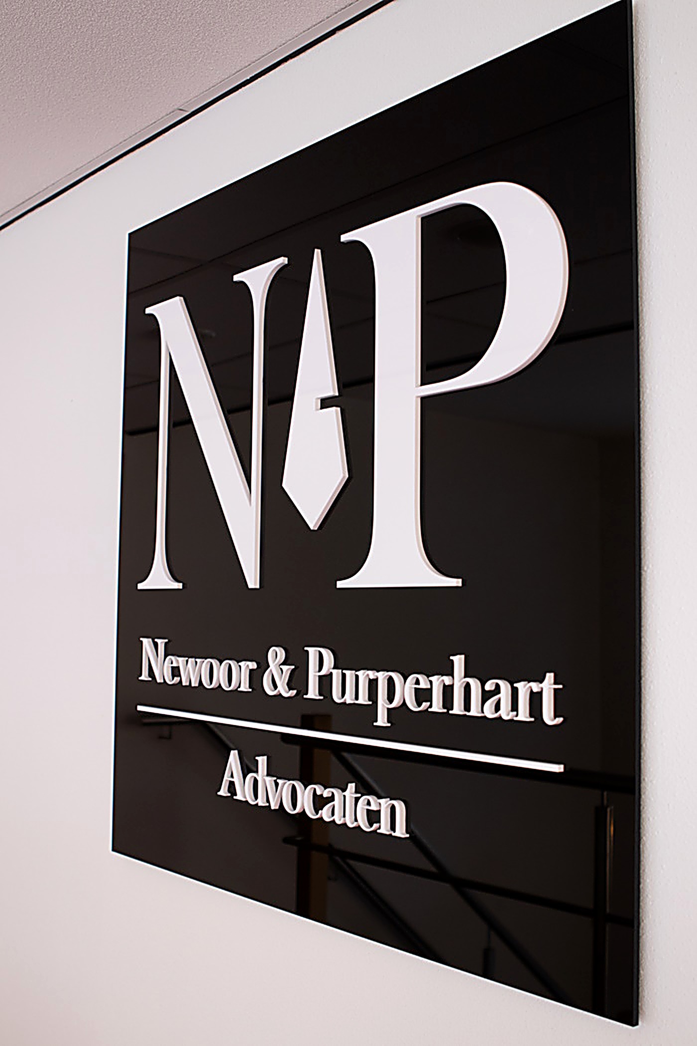 Zwart glazen naambord aan de muur met het witte 3D-logo van Newoor & Purperhart Advocaten